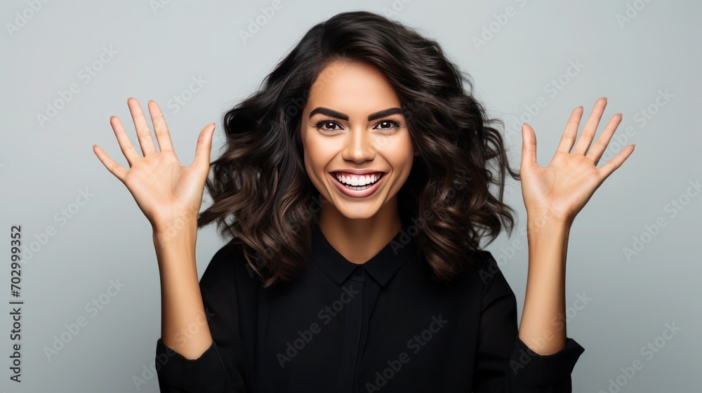 Smiling young Argentine woman with dark curly hair in a black blouse joyfully raises her hands, feigning delight Smiling young Argentine woman with dark curly hair in a black blouse joyfully raises her hands, feigning delight