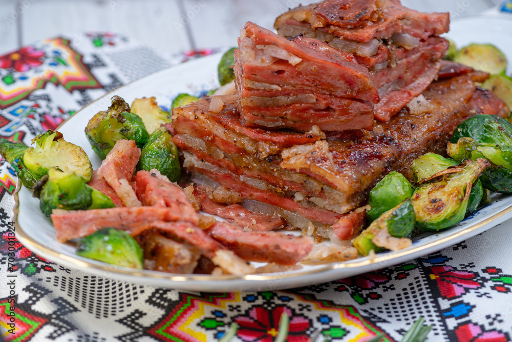 Vegan pork belly roast made with seitan and starch, served on oval plate along with roasted Brussels sprouts. Wooden table, stylish setting