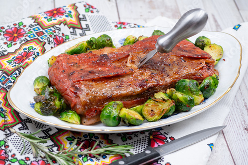 Vegan pork belly roast made with seitan and starch, served on oval plate along with roasted Brussels sprouts. Wooden table, stylish setting