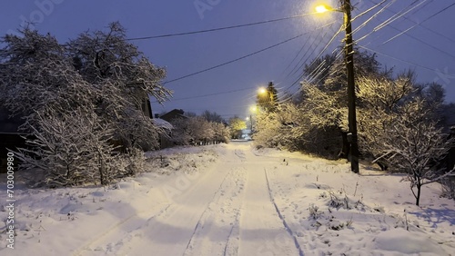 Snowy country road at evening time. Street lamp illuminating snow trail at winter night. Beautiful nature landscape with falling snowflakes at background.
