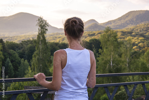 Young woman standing with her back enjoying beautiful natural landscape with mountain view © Alex