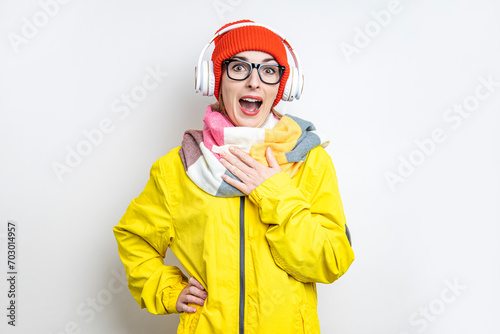 Cheerful surprised young girl in headphones, in a yellow jacket on a light background.