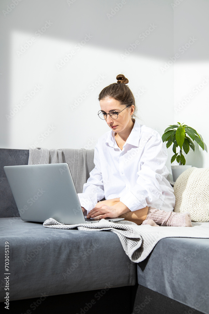 Young woman in glasses working with laptop sitting on sofa. Young woman in glasses working with laptop sitting on sofa.