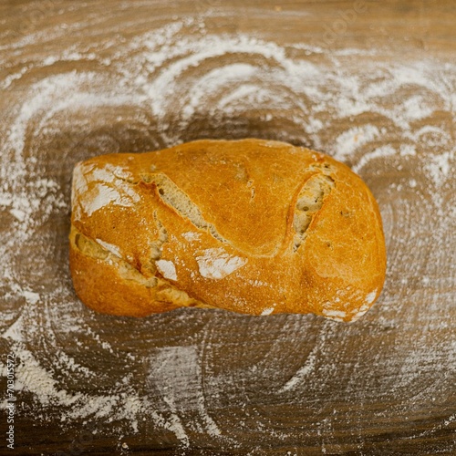 Barra de pan sobre una mesa de madera llena de harina. 
