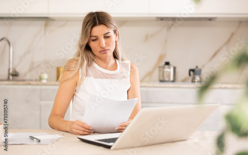 Disappointed woman sitting at table and looking at display of her laptop