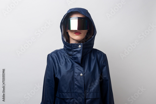 Young woman in virtual reality glasses, in a blue jacket on a light background