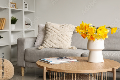 Vase with beautiful narcissus flowers and magazines on coffee table in living room