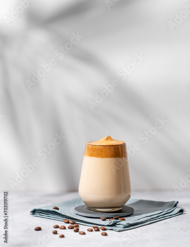 Dalgona coffee. Whipped instant coffee in a glass with beans and shadow on a light background.