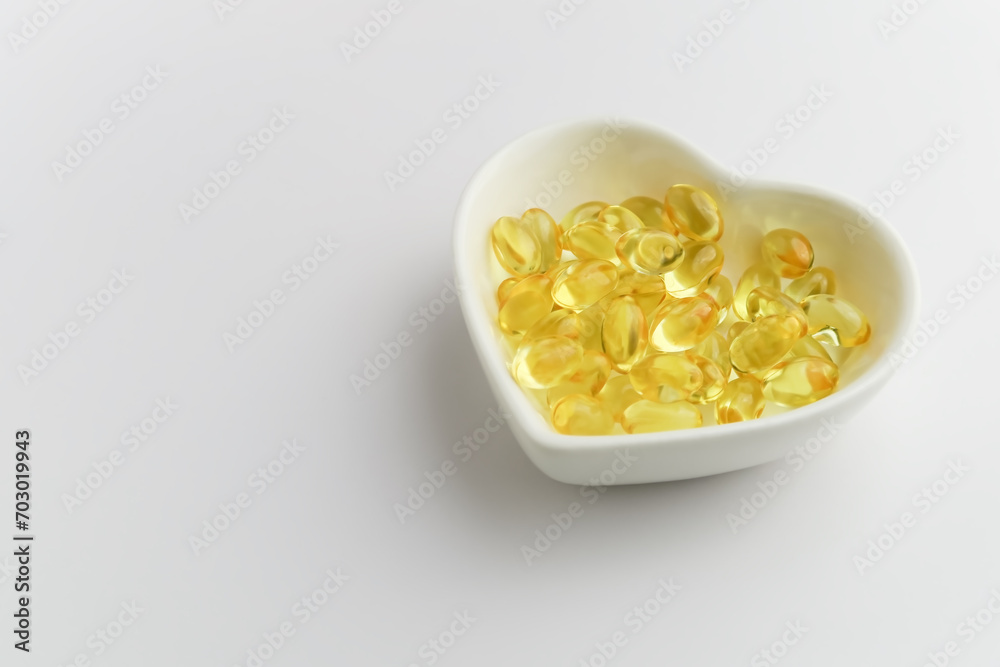 yellow fish oil capsules in a heart shaped plate on a white background yellow fish oil capsules in a heart shaped plate on a white background