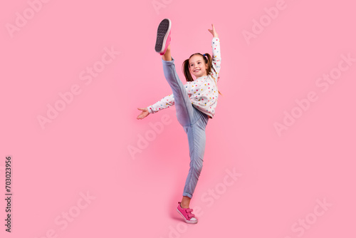 Full length photo of graceful girl wear stylish sweatshirt jeans raising leg up dancing look empty space isolated on pink color background photo