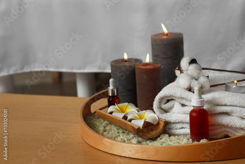 Tray with burning candles  flowers and towels on table in spa salon  closeup