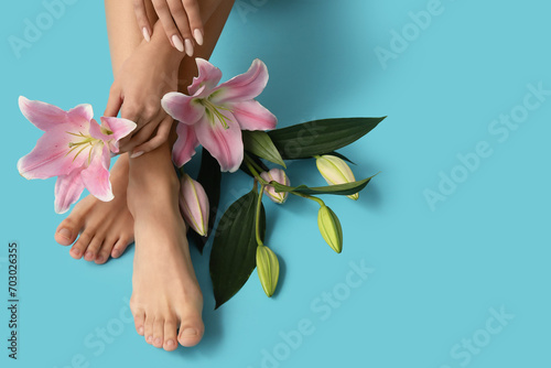 Female feet and hands with beautiful lily flowers on blue background, closeup #703026355