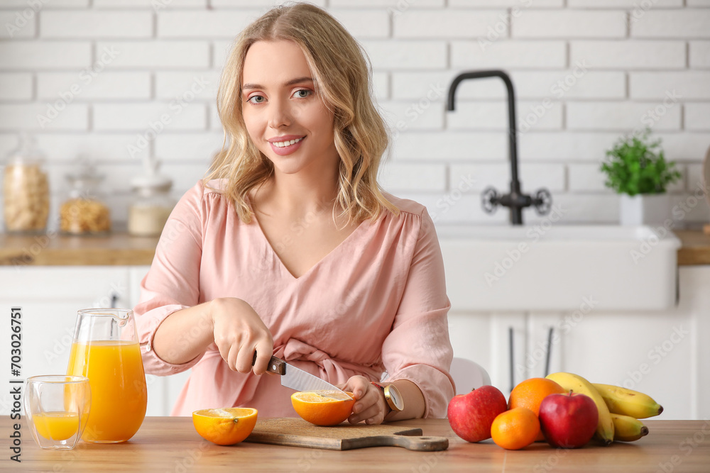 Young pregnant woman cutting orange at table in kitchen