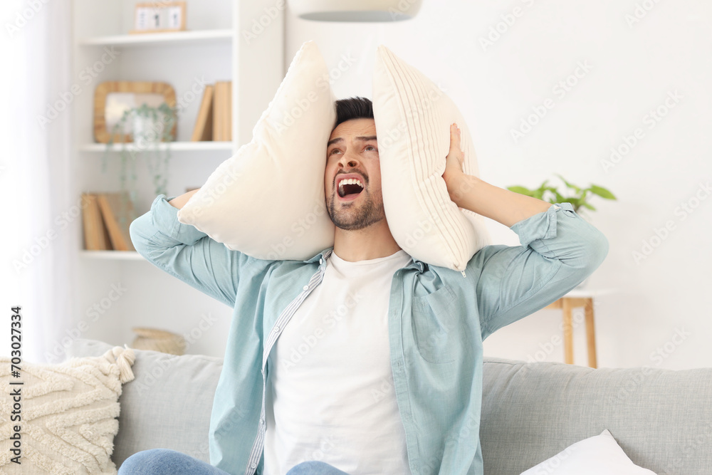Angry young man with pillow suffering from loud neighbours at home