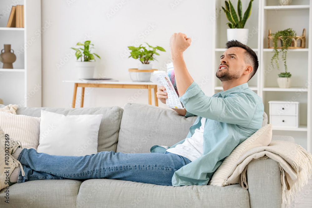 Young man with newspaper suffering from loud neighbours at home Young man with newspaper suffering from loud neighbours at home