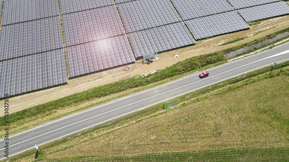 Obraz premium Red electric car with solar panel photovoltaic power plant during a sunny day. Rechargeable lithium battery zero emission alternative sustainable energy