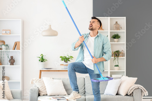 Young man banging ceiling with mop because of loud neighbours at home