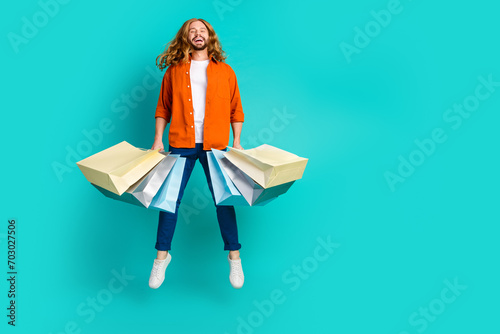 Full body length photo of young energetic funny man shopaholic jumping with pile shopping packages isolated on aquamarine color background