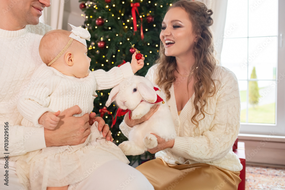 close-up portrait of a beautiful family, father and mother with a little daughter in their arms against the backdrop of a Christmas tree decorated for Christmas and New Year. happy family concept