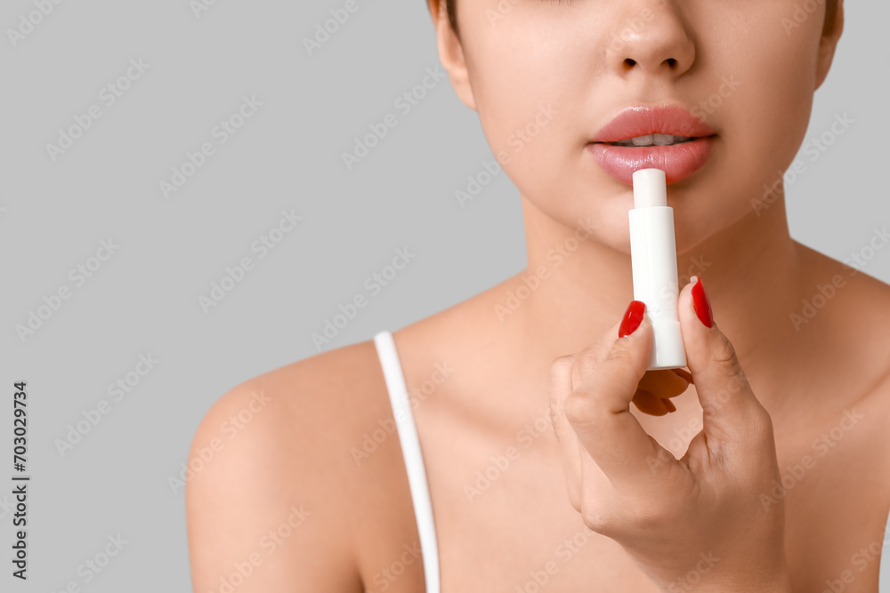 Beautiful young woman applying lip balm on grey background, closeup Beautiful young woman applying lip balm on grey background, closeup