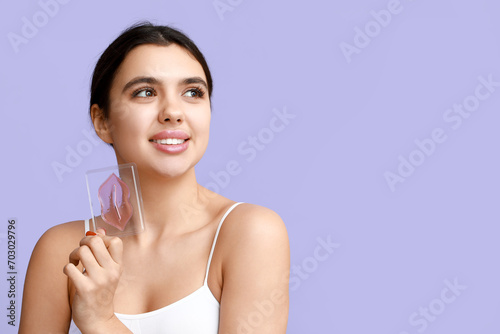 Beautiful young woman with lip mask on lilac background