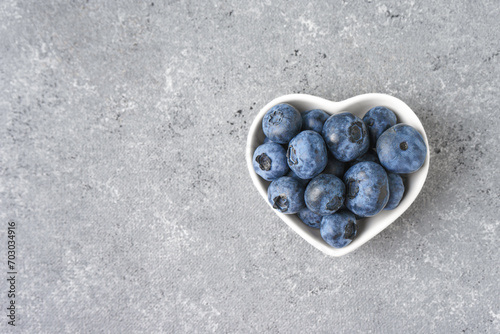 Fresh blueberries in a small heart-shaped bowl on gray concrete background with copy space. Organic berries, healthy food, wild berries. Top view, flat lay