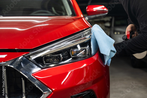 A man washes the headlights of a red car using a microfiber cloth and spray.  © Михаил Решетников
