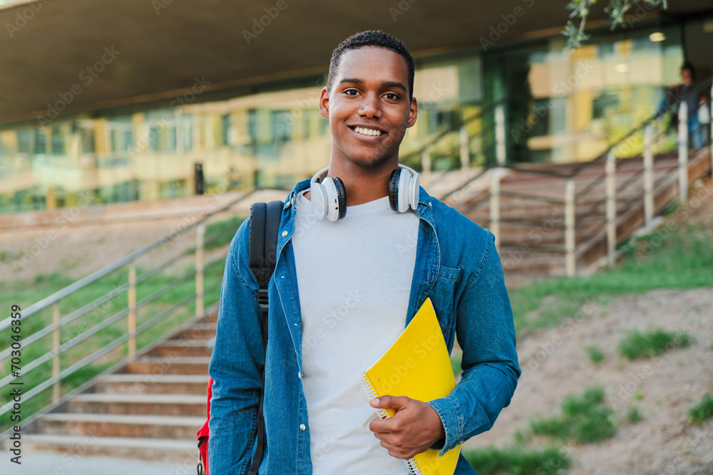 Obraz premium Close up individual portrait of a african american student young man carrying a backpack and note books at university campus. Teenage male smiling and looking at camera. High school guy staring front