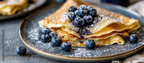 Blueberry crepes topped with powdered sugar on a small grey plate photo