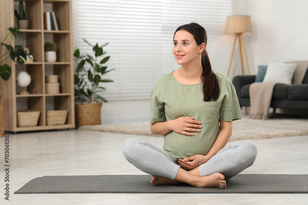 Beautiful pregnant woman sitting on yoga mat at home