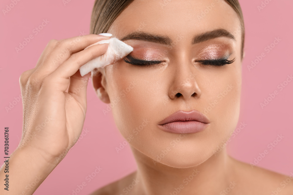 Beautiful woman removing makeup with cotton pad on pink background, closeup