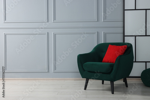 Comfortable armchair with red pillow near light grey wall indoors. Space for text