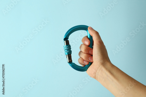 Woman with metal carabiner on light blue background, closeup. Space for text