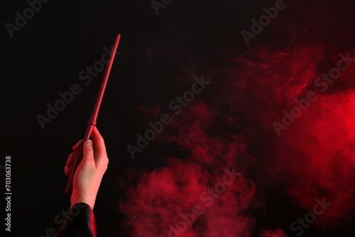 Magician holding wand in smoke on dark background, closeup. Space for text