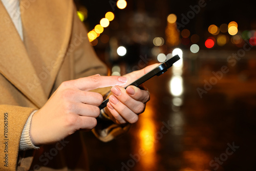 Woman using smartphone on night city street, closeup. Space for text