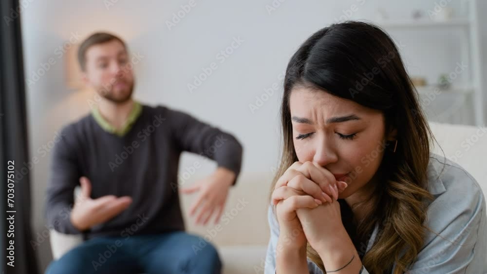 Tired stressed woman sadness looking away sitting on bed on blurred background of aggressive husband shouting on wife at home. Concept of family scandal, crisis, domestic violence, abuse Tired stressed woman sadness looking away sitting on bed on blurred background of aggressive husband shouting on wife at home. Concept of family scandal, crisis, domestic violence, abuse