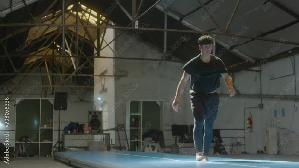 Young male gymnast doing cartwheel and then performing back somersault in slow motion on mat during workout in a gym