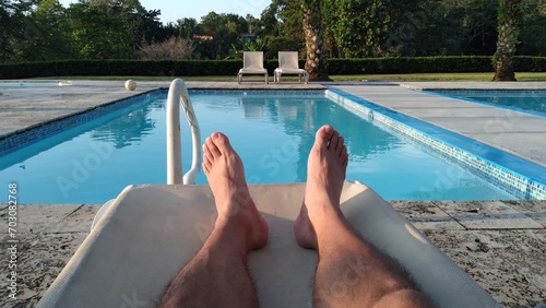 first-person point of view where you can see the legs resting on a chair with the bottom of a pool on a sunny summer day