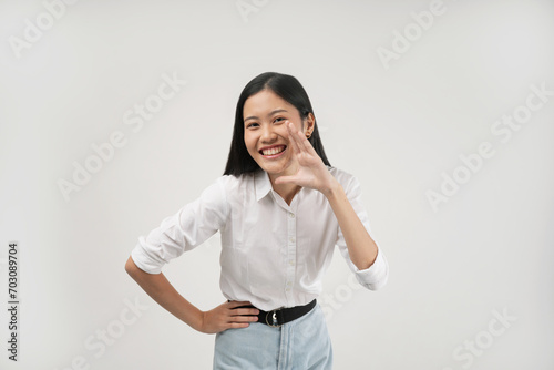 A young Asian woman places one hand on her hip and tilts her head slightly while smiling brightly, exuding confidence and friendliness in a professional setting