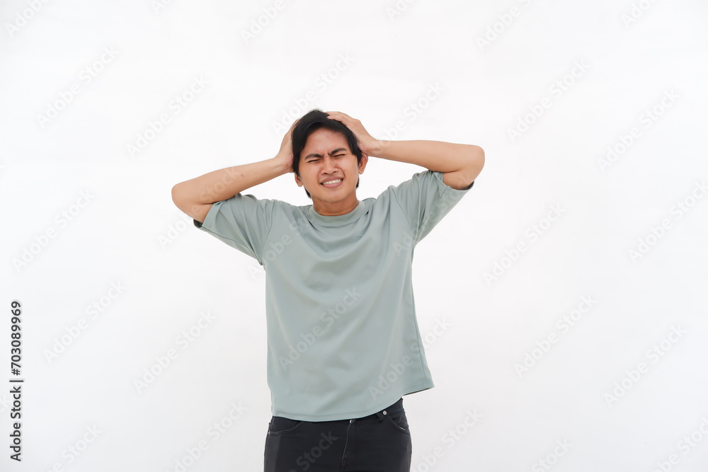 A young Asian man holding his head, experiencing a headache looking confused, depressed, and frustrated A young Asian man holding his head, experiencing a headache looking confused, depressed, and frustrated
