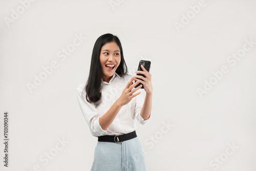 An Asian woman smiles while holding a phone, exuding confidence. Captured in a bright studio, this image aims to represent connectivity and modern lifestyle choices.