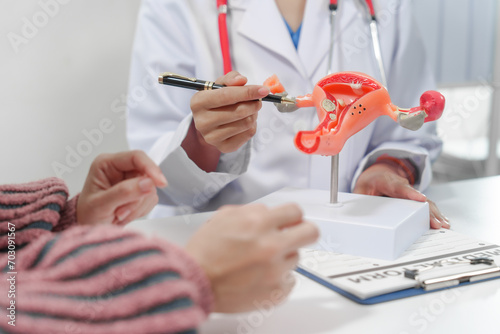 female doctor reassuring patient with comforting hand gesture, with model of the female reproductive system on table, possibly discussing menstruation, cervical cancer, infertility, or sterilization.
