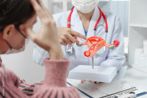 female doctor reassuring patient with comforting hand gesture, with model of the female reproductive system on table, possibly discussing menstruation, cervical cancer, infertility, or sterilization.
