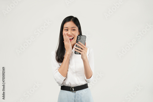 Portrait of a young Asian woman holding her phone feeling excited, shocked having reading news or message and isolated on a white background