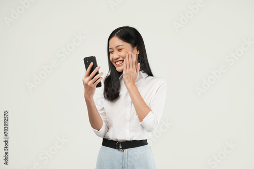 Portrait of a young Asian woman holding her phone feeling excited, shocked having reading news or message and isolated on a white background