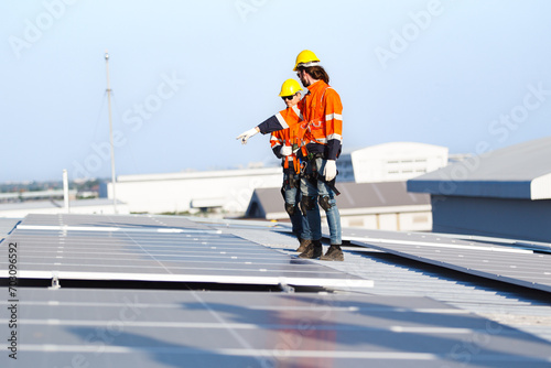 Professional electric engineers survey and inspect solar panels installation on the factory metal sheet roof top.