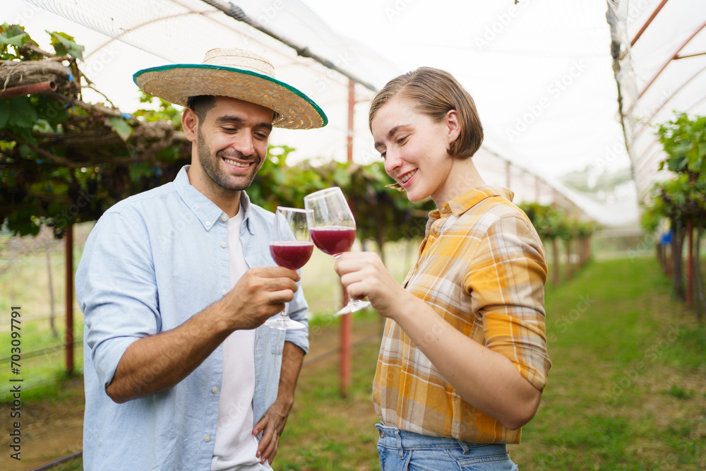 Fototapeta premium Happy vineyard - grape yard farmers tasting a wine or grape juice together while standing in the vineyard. Lovely couple taste a wine - grape juice in the vineyard.