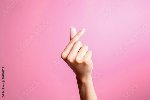 Female hand gesturing showing heart from fingers, korean love symbol over pink background photo