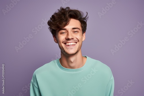 A young guy with a contagious smile in a pale lavender sweater on a light mint-green background.