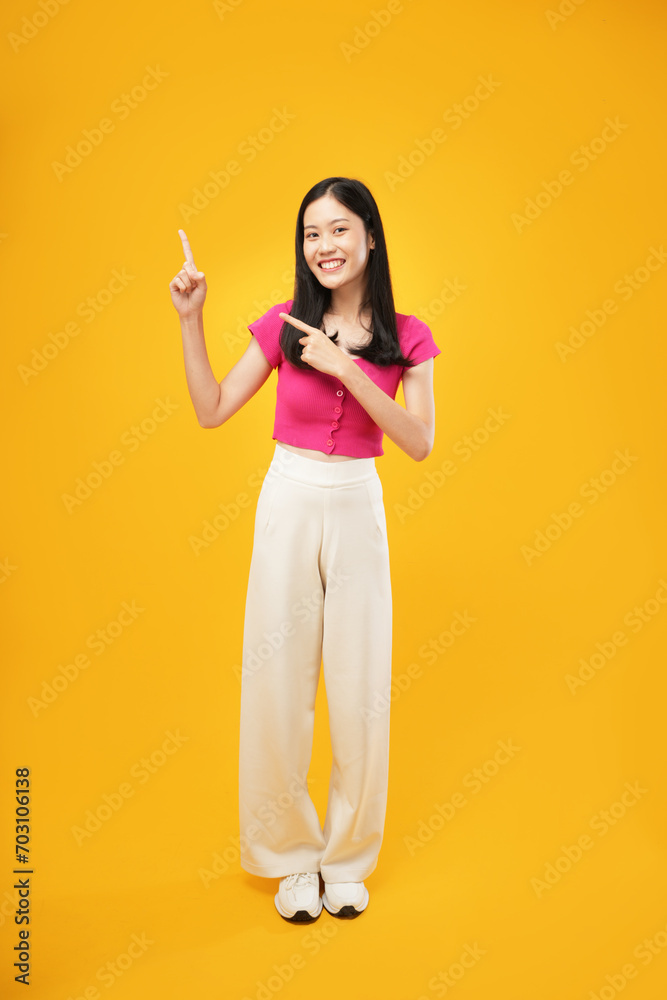 An Asian woman confidently points upward with a thoughtful expression, embodying focus and determination against a vibrant yellow background
